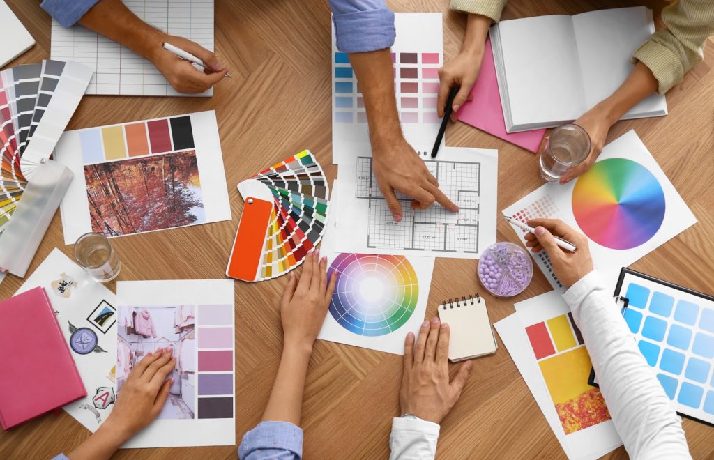 Professional team of graphic designers work at table with color sheets and tables, as seen from a top view. 