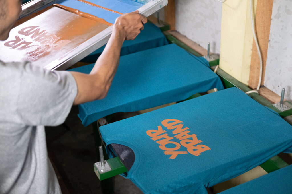 A screen printing tech working on adding the phrase “your brand” on a batch of blue shirts.