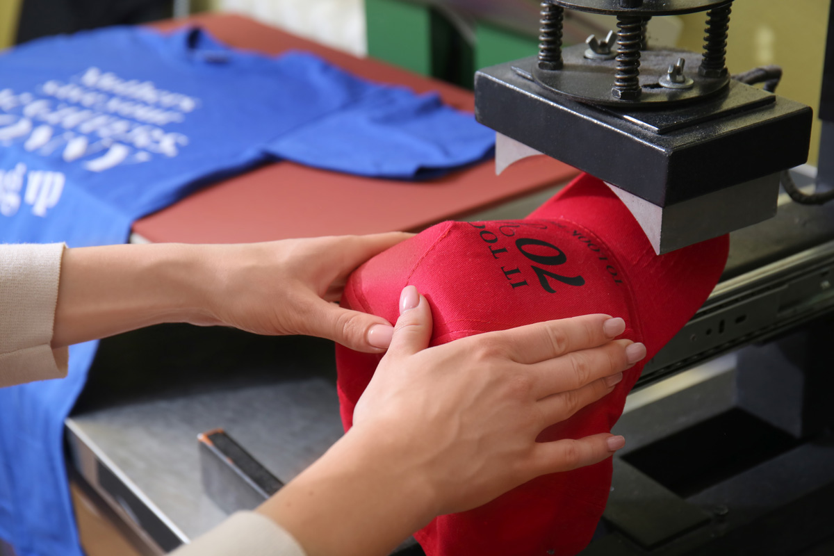 A professional screen printing words onto a red hat in El Paso.