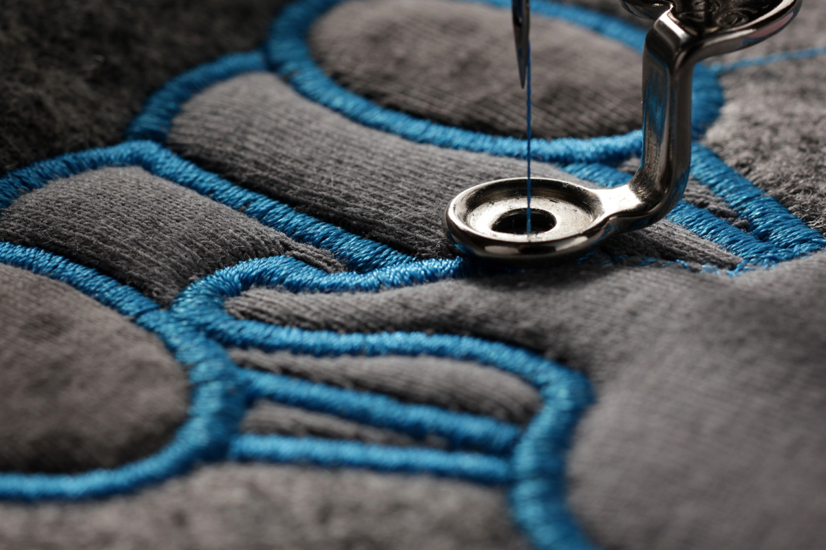 A close-up image of a needle embroidering with blue thread onto a grey fabric in El Paso.