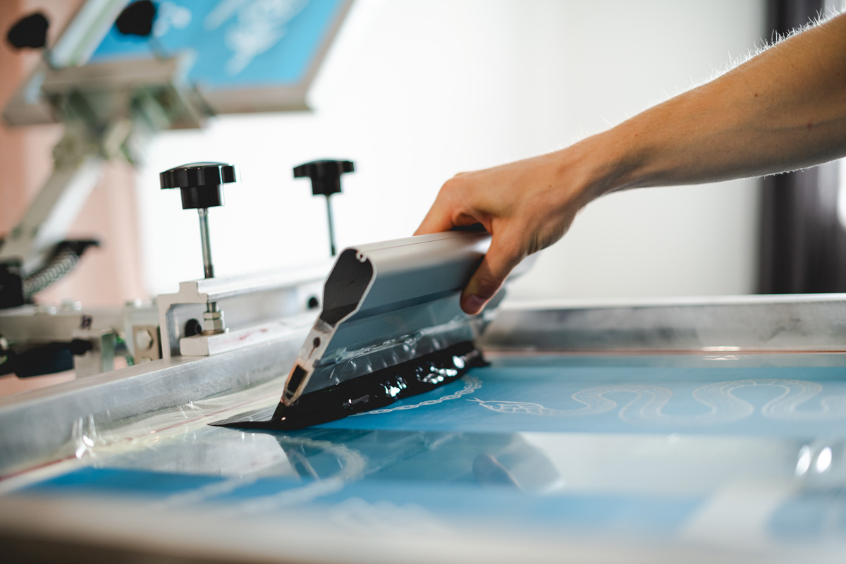 A person’s hand screen printing a product in El Paso.